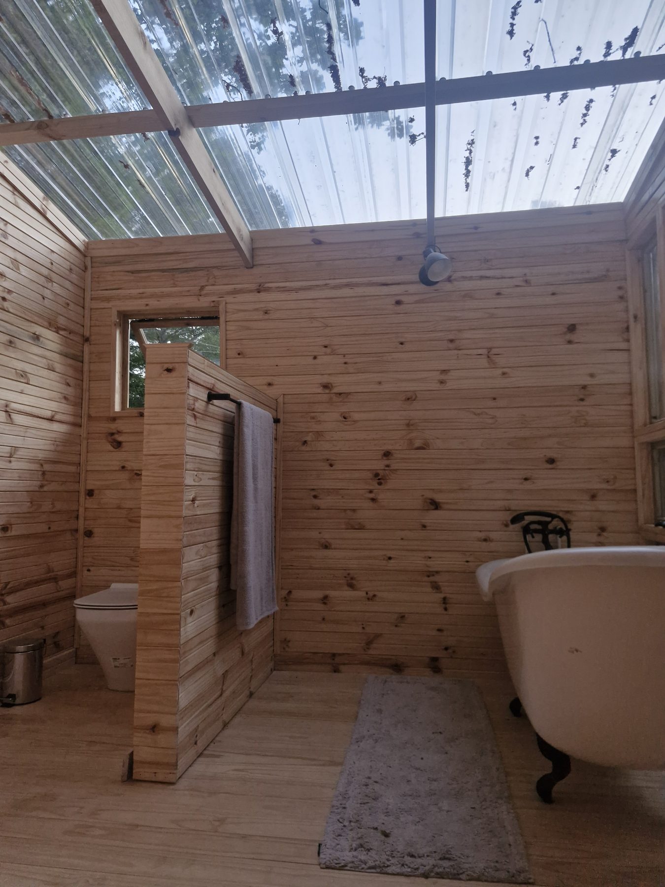The campsite bathroom at Maylodge, Hogsback, with a clear polycarbonate roof open to the trees and a freestanding bath