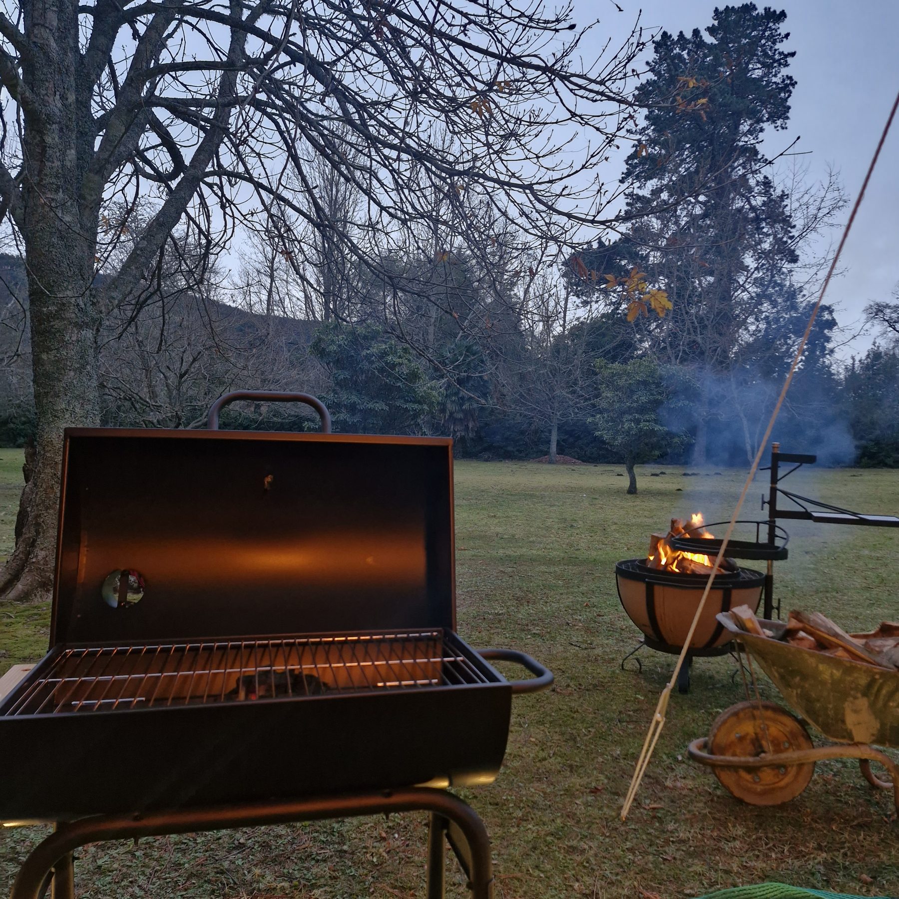 A braai and fire bowl burning on the frosty lawn with a wheelbarrow of firewood at Maylodge campsite